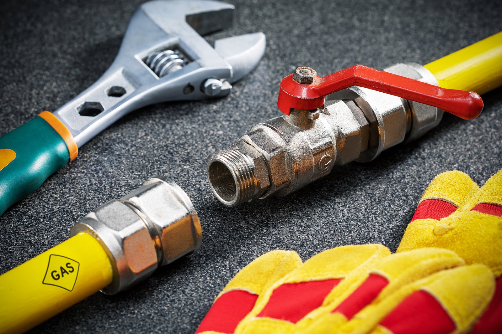 yellow gas pipe, wrench and protective gloves on dark tile surface